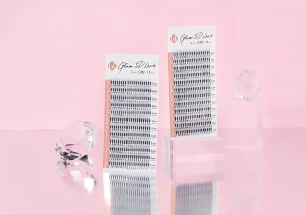 A pair of false lashes on display in front of pink background.